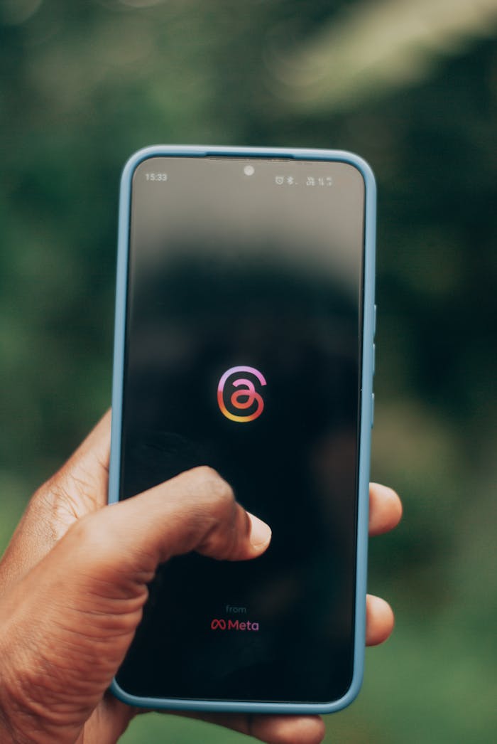 Close-up of a hand holding a smartphone displaying the Meta Threads app against a blurred background.